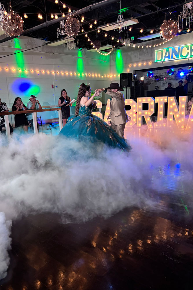 Quince girl celebrating with father and dancing on a lit ballroom dance floor during a lively event reception